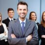 Team leader stands with coworkers in background Team leader stands with coworkers in background